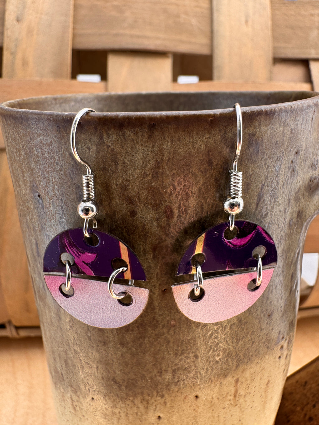 Purple swirl and blush pink two-tone circle drop earrings displayed on a rustic ceramic cup