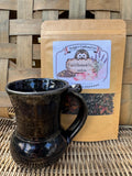 Grå & Blommande Tea bag with a dark glazed ceramic mug on a wicker surface