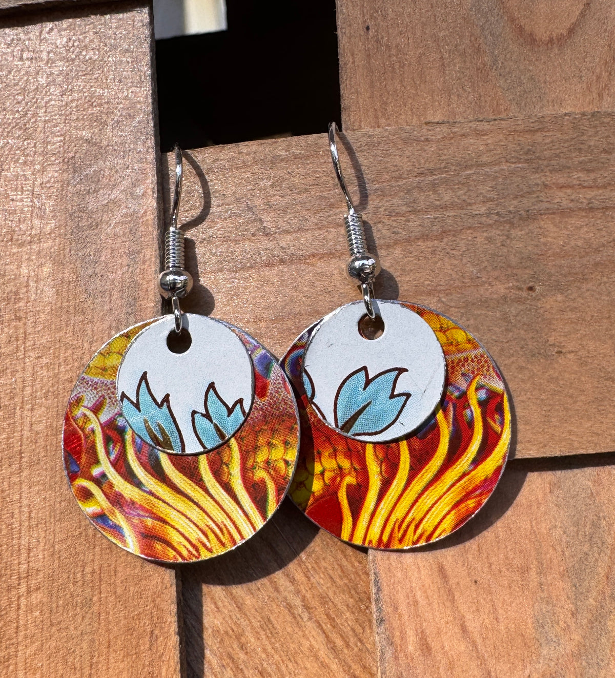Handmade tin circle drop earrings with fiery red orange and gold base disk and white tin overlay with hand-painted blue tulip